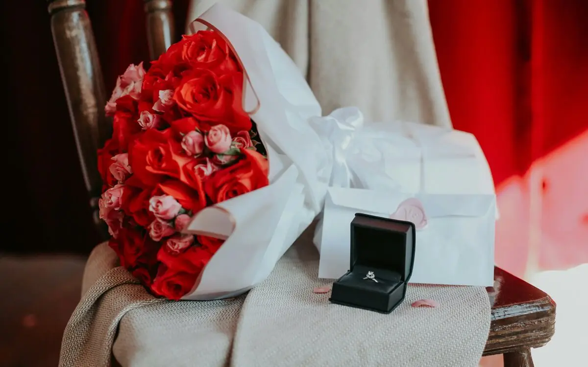 Strauß mit roten Rosen und ein Verlobungsring liegen auf einem Stuhl
